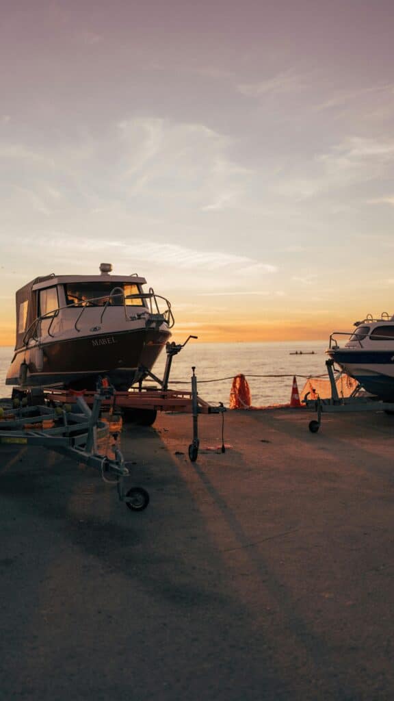 Two boats on trailers by the sea during a vibrant sunset with a calm sky.